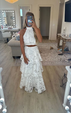 a woman taking a selfie in her living room wearing a white two piece skirt and crop top