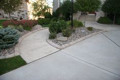 a driveway with landscaping and trees in the background