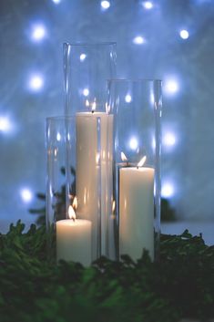 three candles sitting in front of some glass vases filled with greenery and lights