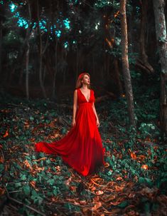 a woman in a red dress is walking through the woods