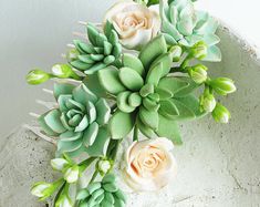 succulents and roses are arranged in a bowl