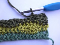 the crochet is being worked on with a blue handled knitting needle in front of it