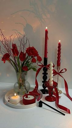 red roses and candles are arranged on a white table with ribbon around the candle holders