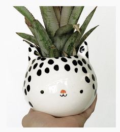 a hand holding a white ceramic pot with black dots and a cat face on it