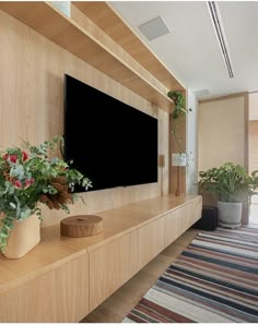 a flat screen tv sitting on top of a wooden shelf next to potted plants