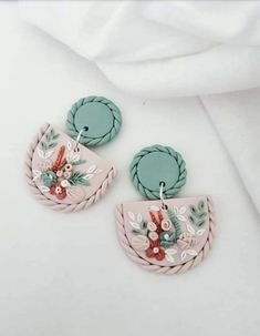 two pink and green earrings with floral designs on the front, one is hanging from a rope