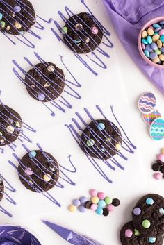 chocolate cookies and candy on a table with purple icing drizzled over them