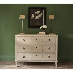 a white dresser sitting in front of a green wall with two lamps on top of it