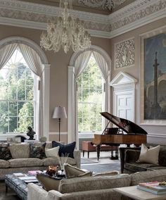 a living room filled with furniture and a grand piano in front of two large windows