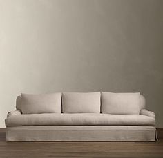 a white couch sitting on top of a hard wood floor next to a lamp and wall