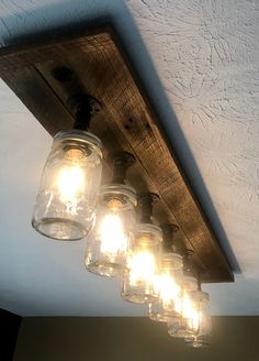 mason jars are hanging from the ceiling in this rustic style light fixture, which is made out of wood planks