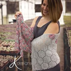 a woman holding up a sweater in a greenhouse