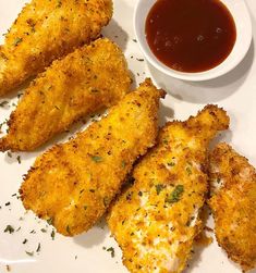 some fried food on a white plate next to a small bowl of sauce and ketchup