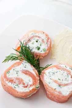 salmon roll with cream cheese and dill sprig on white plate next to potato wedges