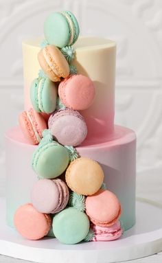 a three tiered cake with macaroons on the top and bottom layer in pastel colors