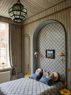 a bed room with a neatly made bed next to a window and a hanging lamp