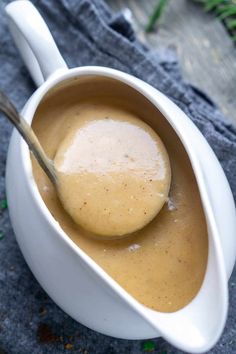 a spoon in a white bowl filled with gravy on top of a table