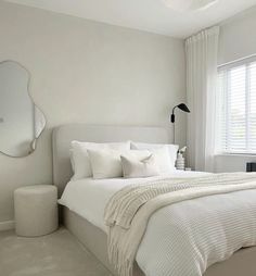 a white bedroom with a large bed and mirror on the wall, along with two stools