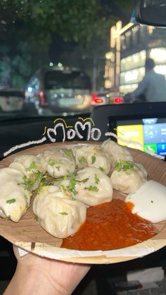 a person holding a plate with dumplings and sauce on it in front of a car