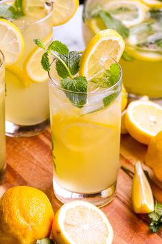 two glasses filled with lemonade and mint on top of a cutting board next to sliced lemons