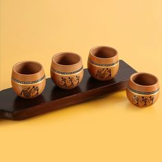 four brown bowls sitting on top of a wooden tray next to an orange wall and yellow background