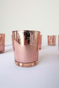 several pink candles are lined up on a white tablecloth and one candle has gold speckles