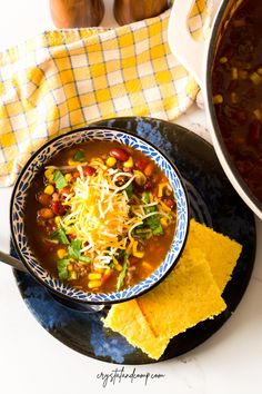 a bowl of chili and corn soup with tortilla chips next to it on a plate