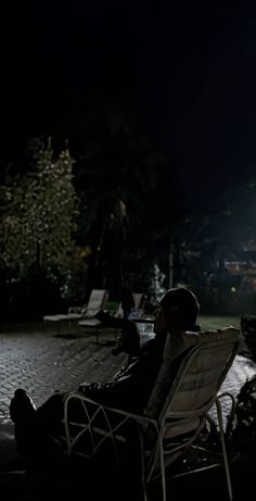 a man sitting in a lawn chair at night with his feet up on the ground