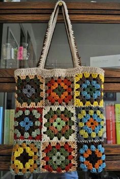 a multicolored crocheted bag hanging from a book shelf with books behind it