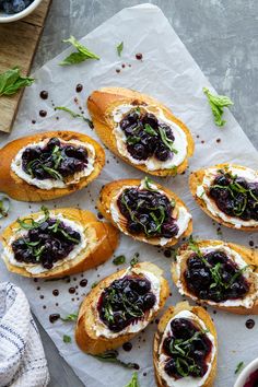 small crostini with blueberries and cream cheese on top sitting on a piece of parchment paper