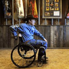 a man sitting in a wheel chair wearing a cowboy hat and blue shirt with his hands on his hips