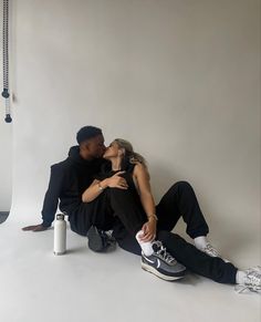 a man and woman sitting next to each other in front of a white background kissing