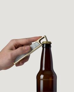 a person opening a bottle opener on top of a brown beer bottle in front of a white background