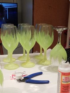 green wine glasses sitting on top of a white table next to scissors and other items