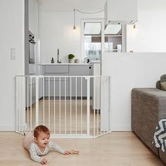 a baby crawling on the floor in front of a white gated living room area