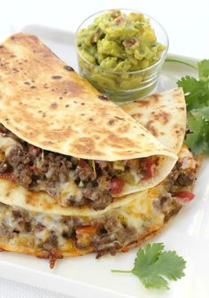 three quesadillas on a white plate with guacamole and salsa