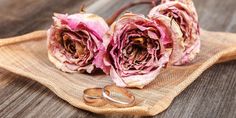 two wedding rings are sitting on a cloth with pink flowers in the middle and one ring is laying next to it