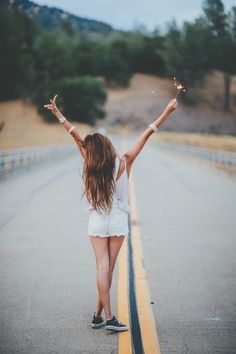 a woman is walking down the road with her arms in the air while holding two sparklers