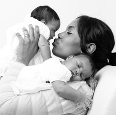 a woman laying on top of a couch holding a baby and kissing her face with both hands