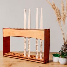 a wooden rack with six candles on it next to a potted plant and vase