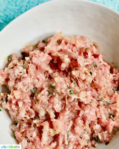 a white bowl filled with tuna salad on top of a blue towel next to a spoon