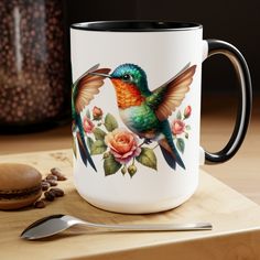 a hummingbird painted on a coffee mug next to a spoon and cup with beans