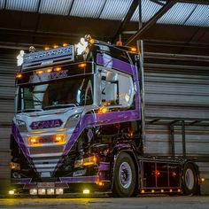 a purple semi truck parked in front of a garage door with lights on it's side