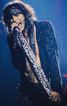 a man with long hair and no shirt on holding a microphone in front of his face