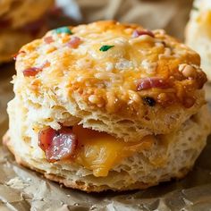 two biscuits with cheese, bacon and other toppings on them sitting on wax paper