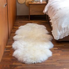 a white sheepskin rug is on the floor in front of a bed and nightstand