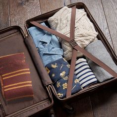 an open suitcase filled with clothes on top of a wooden floor next to a pair of socks