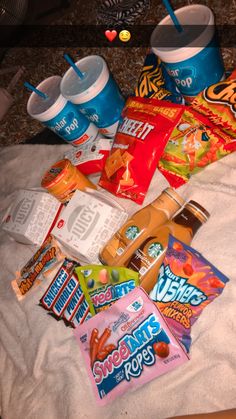 various snacks and drinks on a bed next to each other with candy bars in them