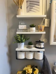 a bathroom with two shelves holding toilet paper rolls and yellow flowers on the shelf next to it