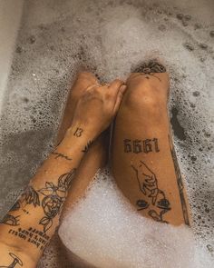 two people are sitting in the bathtub with tattoos on their legs and feet, both holding each other's hands